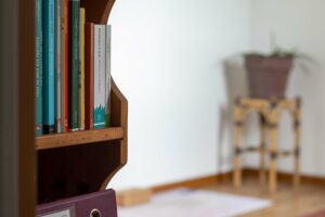 Étagère en bois remplie de livres sur le yoga, avec une plante en pot floue en arrière-plan.